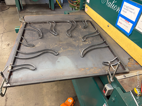 The frame with tentacles is clamped to the sheet on the in-feed of the hydraulic shear. This is so that the exact edges can be scribed onto the sheet, while the already-placed corners are in their final places